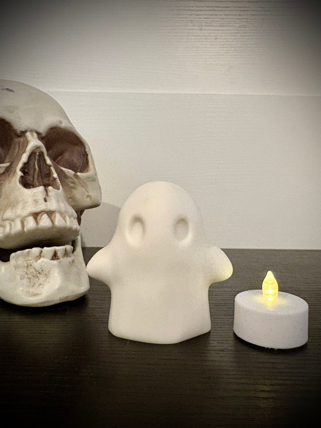 Ghost votive cover shown unlit beside a flickering tea light and skull
